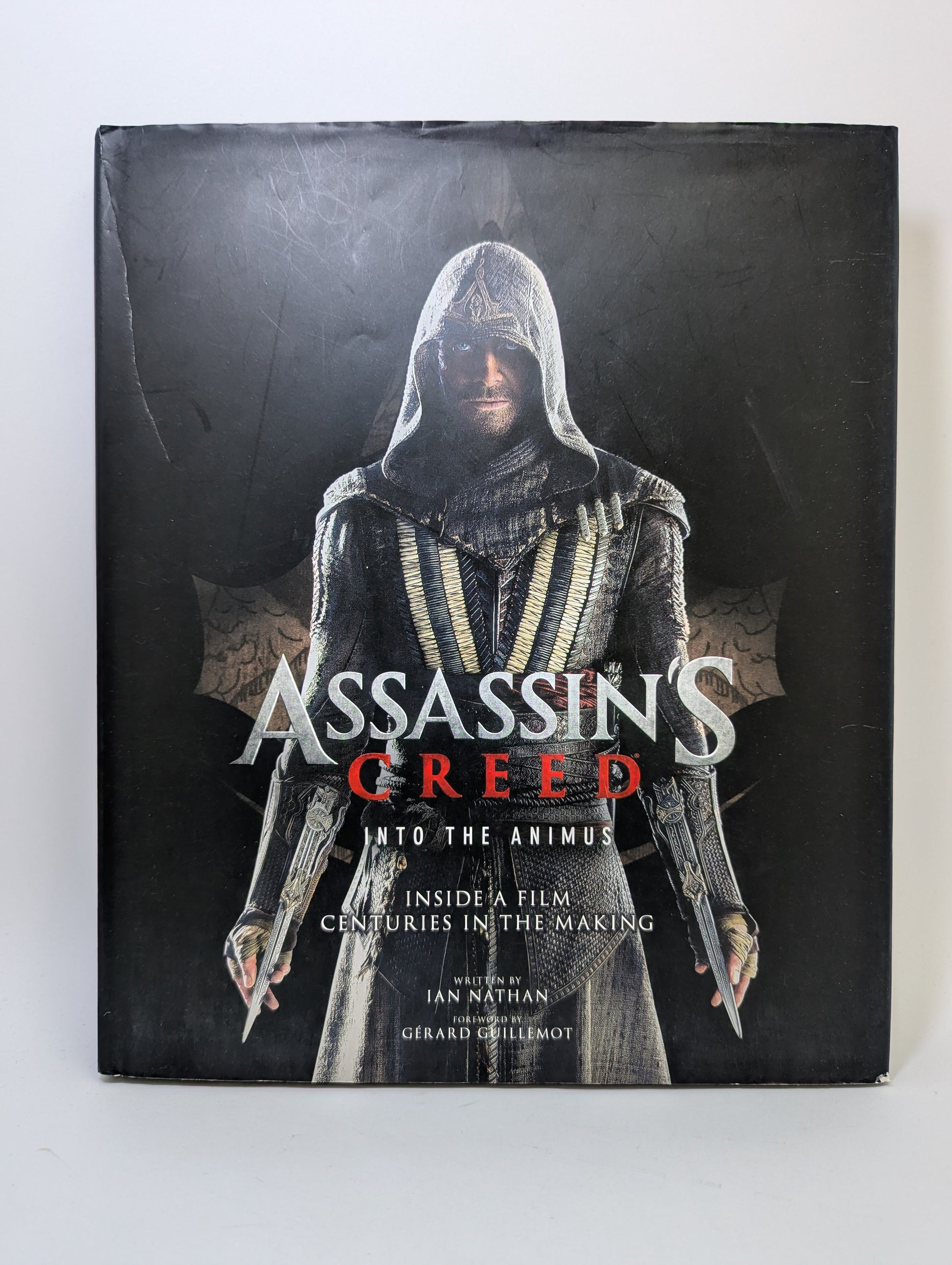Meno knygos Assassin’s Creed: Into the Animus viršelis su žaidimo personažų ir istorinių aplinkų iliustracijomis.