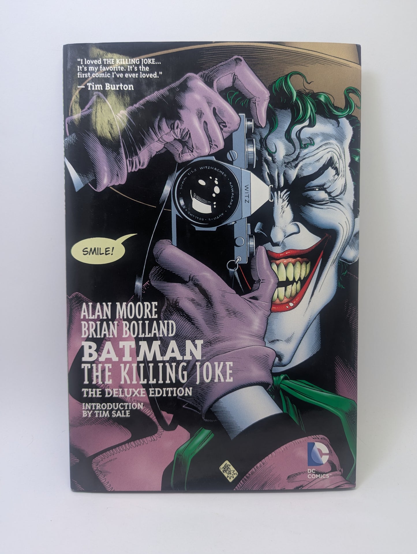 „Batman: The Killing Joke“ grafinės novelės viršelis su besijuokiančiu Džokeriu, laikančiu fotoaparatą.