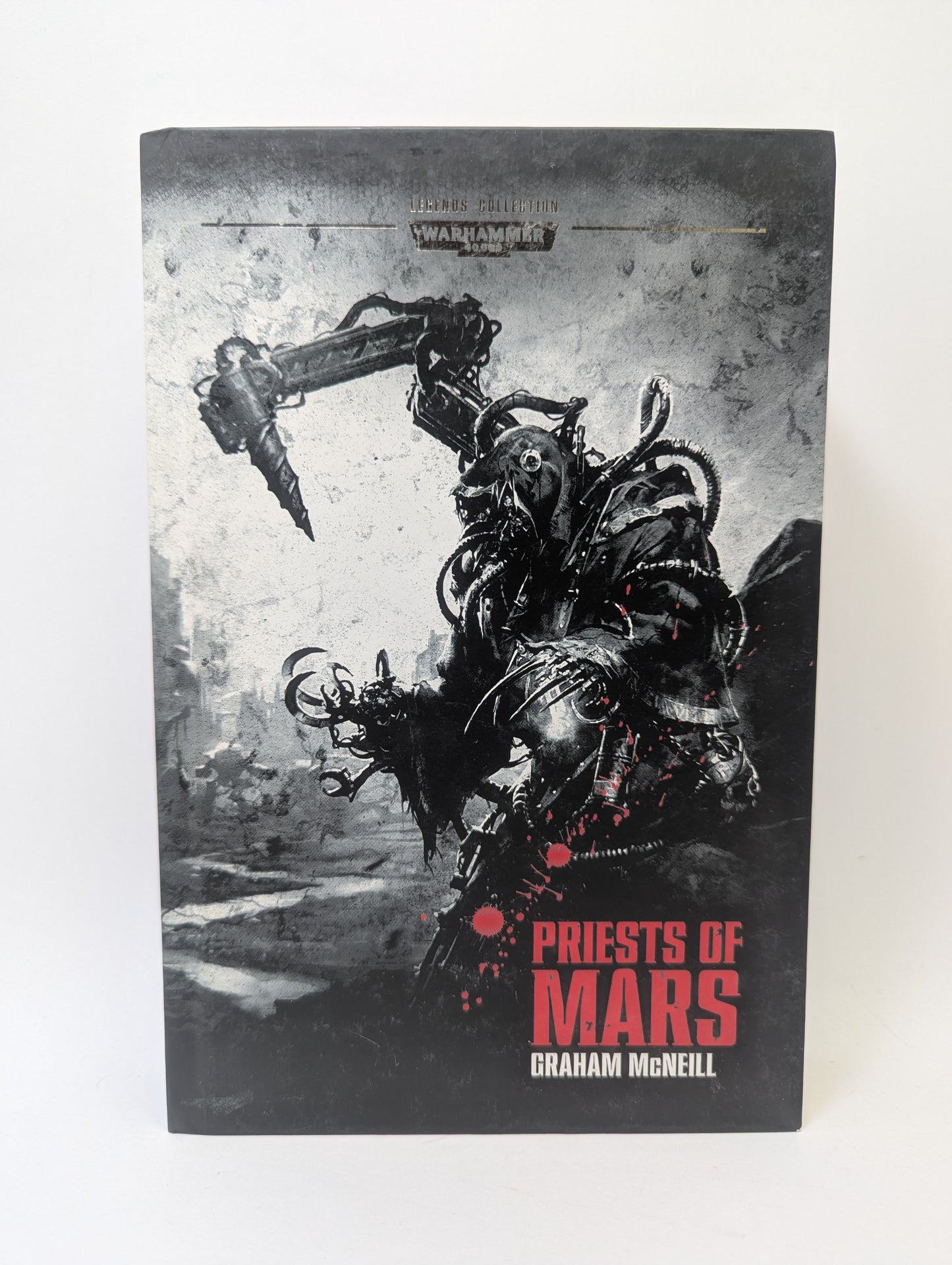 Warhammer 40K knyga „Legends Collection Book 55 – Priests of Mars“ su Adeptus Mechanicus simbolika ir grimdark mokslinės fantastikos viršeliu.