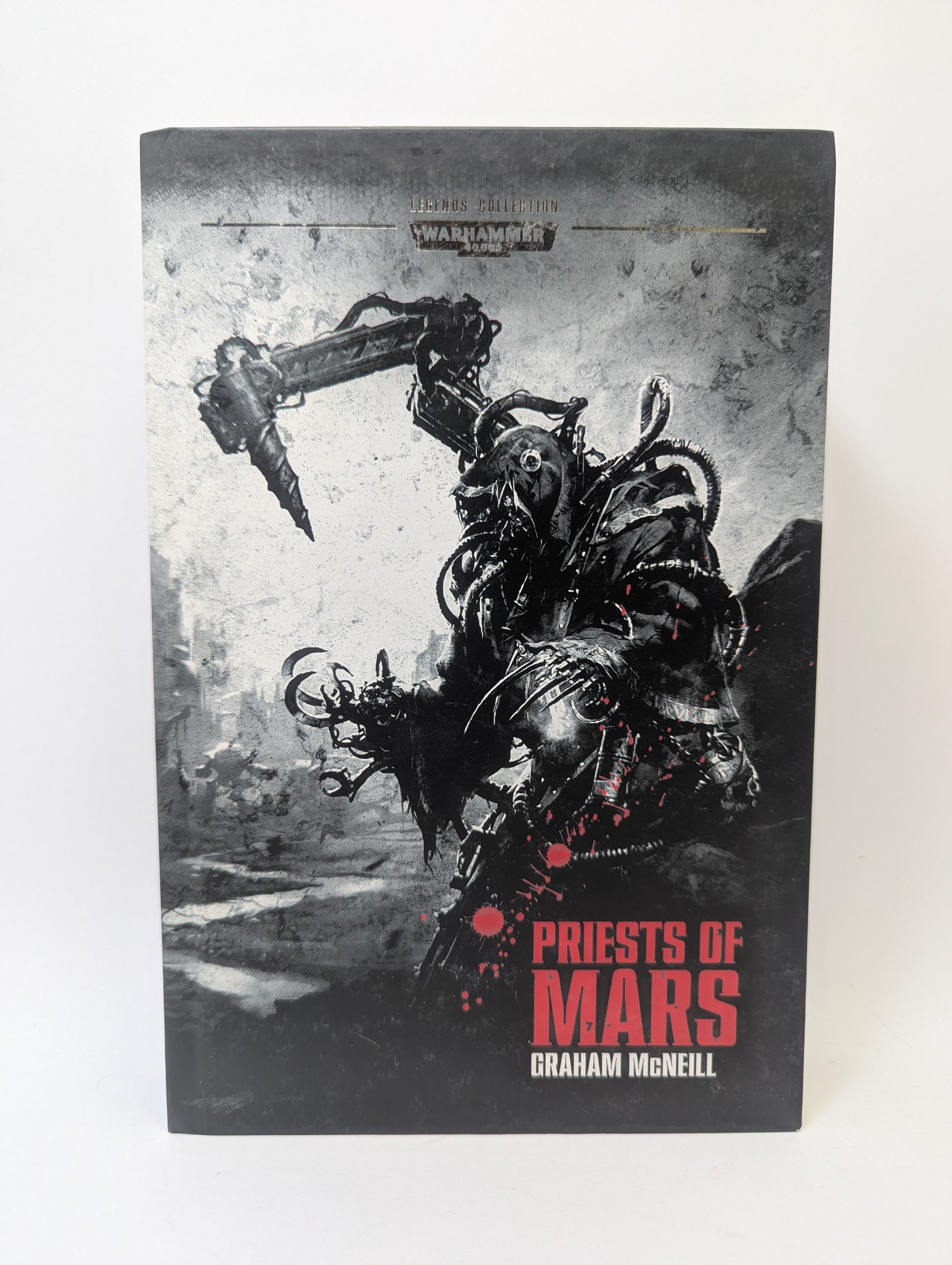 Warhammer 40K knyga „Legends Collection Book 55 – Priests of Mars“ su Adeptus Mechanicus simbolika ir grimdark mokslinės fantastikos viršeliu.